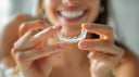 Woman holding her clear replacement retainer at a bathroom mirror — NewSmile reorder kit for American customers