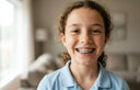 Child smiling confidently while wearing metal braces
