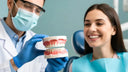 Dentist showing dental crown model to smiling patient