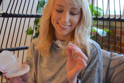 Woman showing a clear NewSmile Night Guard for teeth grinding with protective storage case.