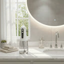 White electric toothbrush on a bathroom counter with a large round mirror and window in the background.