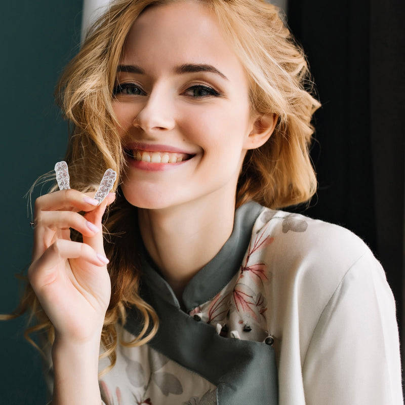 a woman holding a clear aligner while smiling